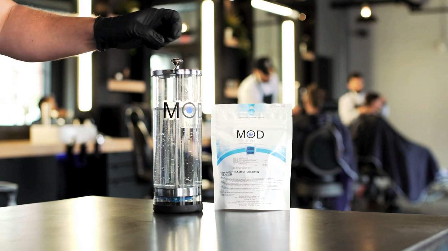 Load video: Demonstration of a MOD pod being dropped into a disinfectant jar. After a about 20 seconds the pod begins to dissolve and the user lifts the lid/basket to mix the solution into a perfectly blended blue disinfectant.